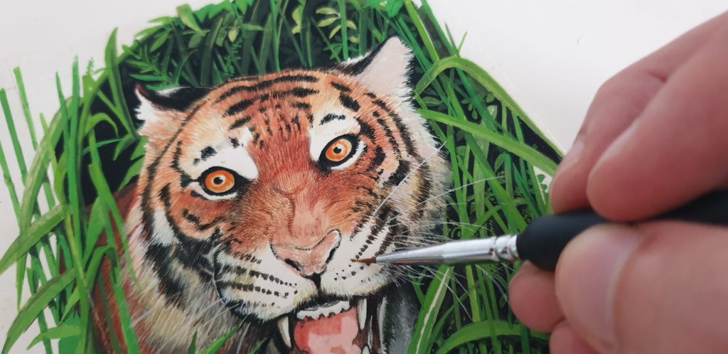 a man's hand painting a tiger in grass with a fine detailed brush