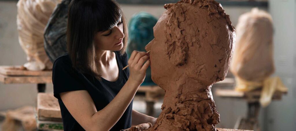 artist with short dark hair detailing a face sculpture