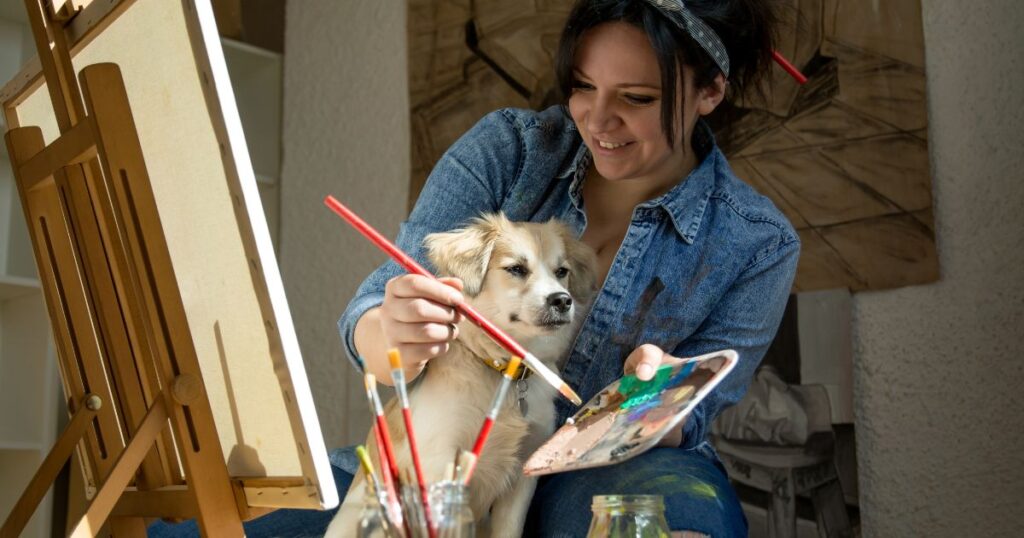 an artist sitting at a canvas painting with a dog