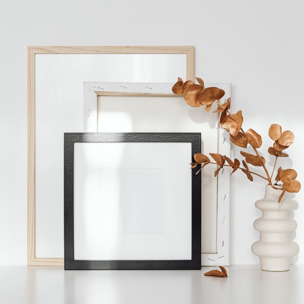 a white background with a canvas and two picture frames. To the right is a modern vase with bronze leaves in. Certificate of authenticity article