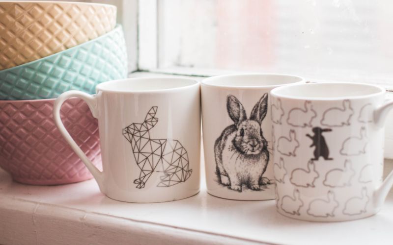 three coloured bowls next to three mugs featuring licensing illustrations from artists